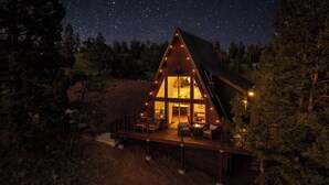 A cabin with a deck, a large window, and a starry night sky. - The Timber Triangle-Views, Hot tub, Firepit (Florissant)