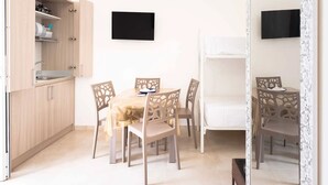 A compact room with a kitchenette, a dining table with chairs, a flat-screen TV mounted on the wall, and a white bed. - Monolocale Alba Salentina Nuovo, Elegante e Vicino al Mare (Nardò)