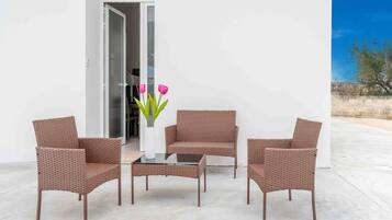 A patio with wicker furniture, a glass table, and a vase with flowers.