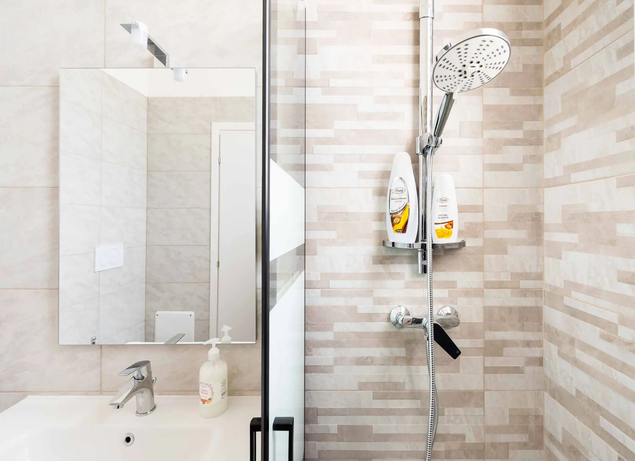 Un baño moderno con cabina de ducha de vidrio, un lavabo con dispensador de jabón y un espejo.