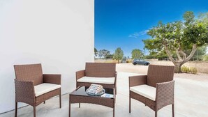 A patio with wicker furniture and a glass table, overlooking a parking area and trees. - Monolocale Alba Salentina Nuovo, Elegante e Vicino al Mare (Nardò)