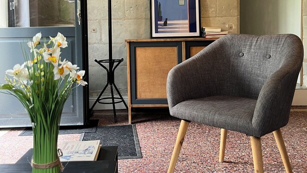 A room with a grey armchair, a framed picture on a wooden cabinet, a vase of flowers, and a black coat rack. - New 2-⭐️ cottage on a Loire island, ideal for families (Gennes-Val-de-Loire)