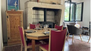 A dining area with a stone fireplace, wooden table, red chairs, and a view of greenery outside. - New 2-⭐️ cottage on a Loire island, ideal for families (Gennes-Val-de-Loire)