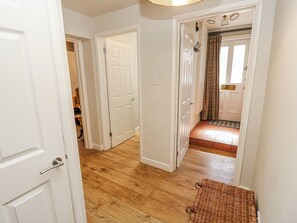 A hallway with wooden flooring, white doors, and a wicker bench. - Clifton Lodge (Winchester)