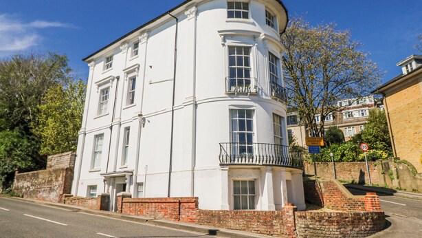 A white, two-story building with a curved corner, a brick base, and a small balcony on the second floor. - Clifton Lodge (Winchester)