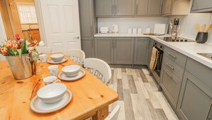 A modern kitchen with grey cabinets, a wooden dining table set with plates and cups, and a vase of tulips. - Clifton Lodge (Winchester)