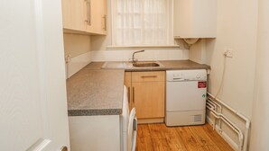 A compact kitchen with a sink, a dishwasher, and wooden cabinets. - Clifton Lodge (Winchester)