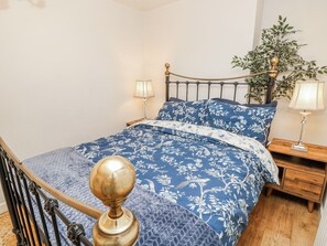 A bedroom with a bed, two bedside tables, a nightstand, a lamp, a potted plant, and a wooden staircase. - Clifton Lodge (Winchester)