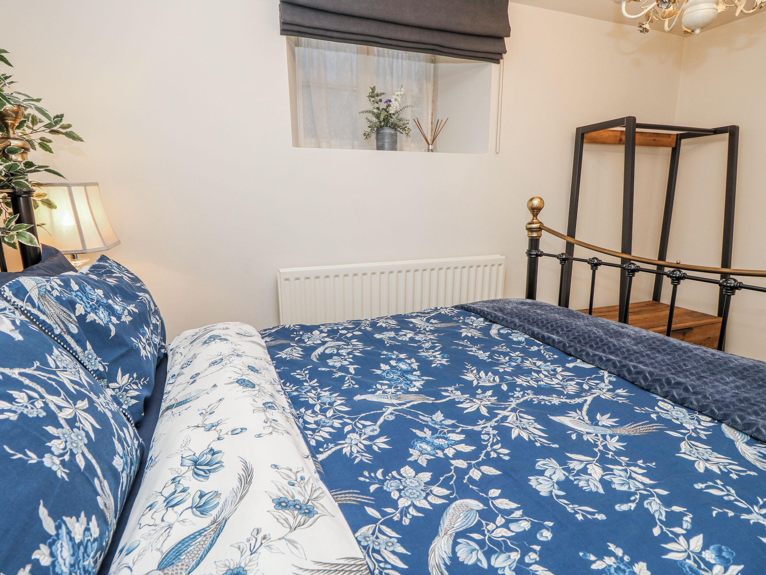 Een slaapkamer met een bed, nachtkastje, lamp, raam met uitzicht en een radiator.