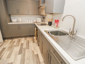A modern kitchen with grey cabinets, a stainless steel sink, and a herringbone-patterned floor.