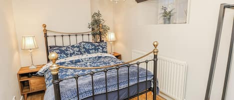A bedroom with a bed, bedside tables, a radiator, a window with a view, and a chandelier.