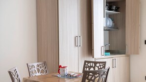 A dining area with a table set for four, surrounded by chairs with intricate back designs. A cabinet with a glass door is visible in the background, containing kitchenware. - Monolocale Riva Wi-fi, Clima e Giardino a Torre Lapillo (Nardò)