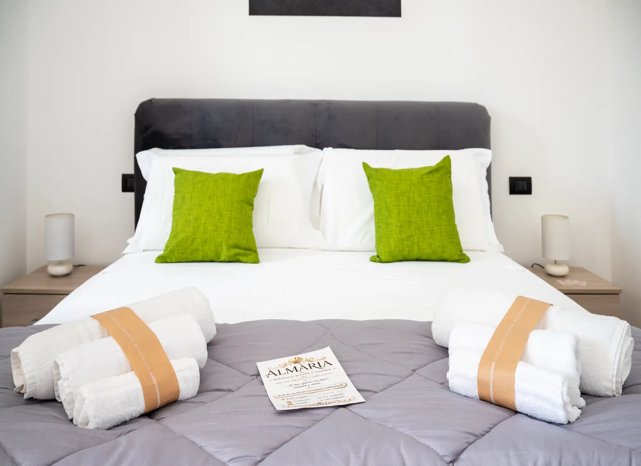 A neatly made bed with white and green pillows, a grey headboard, and two bedside tables with lamps.