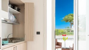 A modern kitchen with a built-in sink and cabinets, a dining area with wicker chairs and a table, and a view of a balcony with a tree and tulips. - Monolocale Riva Wi-fi, Clima e Giardino a Torre Lapillo (Nardò)