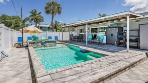 Piscina com deck revestido, área de varanda coberta com cadeiras e um pequeno edifício com garagem.