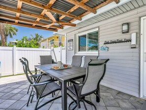 A covered patio with a table and chairs, a sign for pool rules, and a sign for pool towels. - Pearl Beach House - Walk to FMB, Pool & Hot Tub! (Fort Myers Beach)