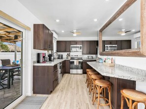 A modern kitchen with dark cabinets, stainless steel appliances, a marble countertop, and a bar area with stools. - Pearl Beach House - Walk to FMB, Pool & Hot Tub! (Fort Myers Beach)