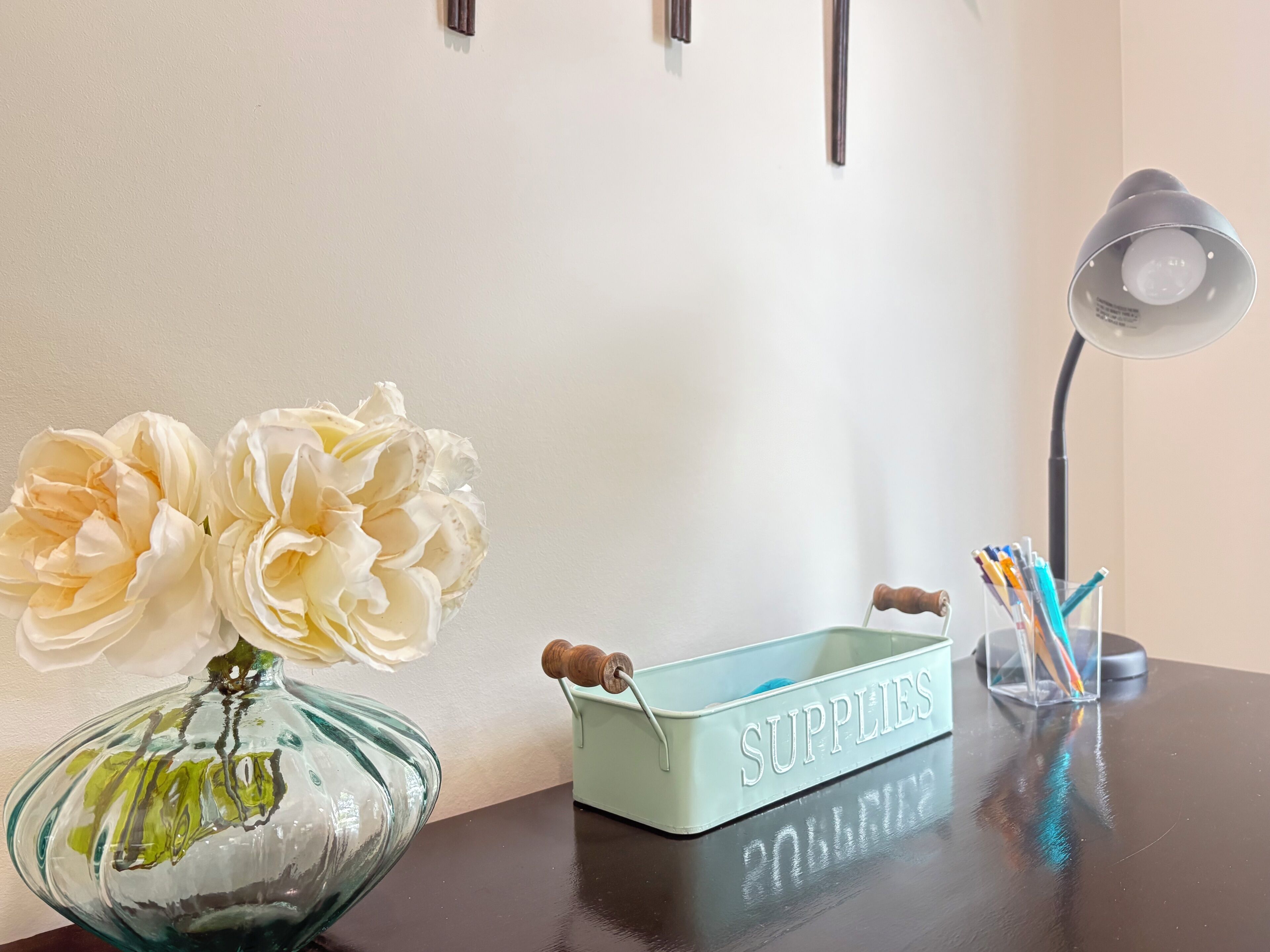 A desk with a vase of flowers, a supplies box, and a desk lamp.