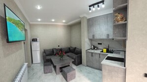 A compact living space with a sofa, coffee table, kitchen area, and a flat-screen TV mounted on the wall. - Livana Guesthouse  (Goris)