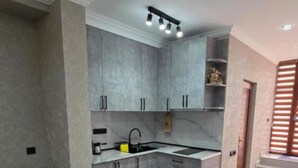 A modern kitchen with grey cabinets, a built-in oven, and a dining area with a table and chairs. - Livana Guesthouse  (Goris)