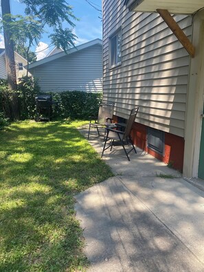 Un jardin à l’arrière d’une maison, avec une terrasse, un barbecue et un banc en bois.