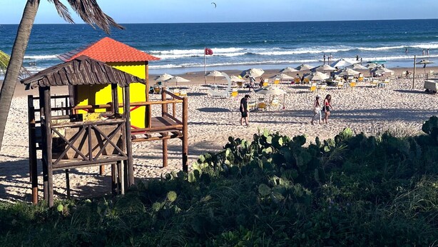 Una playa con una torre de salvavidas, sombrillas y gente.