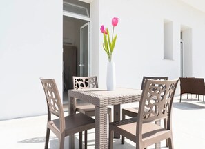 An outdoor dining area with a table and chairs, a white vase with flowers, and a white wall. - Monolocale Vela Nuovo con Wi-fi, Clima e Giardino a Torre Lapillo (Nardò)