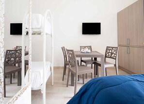 A bedroom with a bed, a bedside table, a chair, a small table with a cup and saucer, a wardrobe, and two wall-mounted TVs. - Monolocale Vela Nuovo con Wi-fi, Clima e Giardino a Torre Lapillo (Nardò)