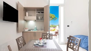 A modern kitchen with a dining area, a TV mounted on the wall, and a view of a garden through an open door. - Monolocale Vela Nuovo con Wi-fi, Clima e Giardino a Torre Lapillo (Nardò)