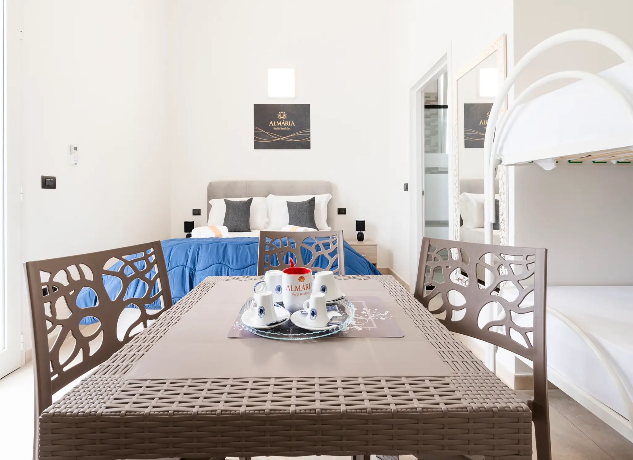 Una camera d'albergo con un letto, un tavolo con prodotti per la colazione, un cartello appeso al muro e un letto a castello.