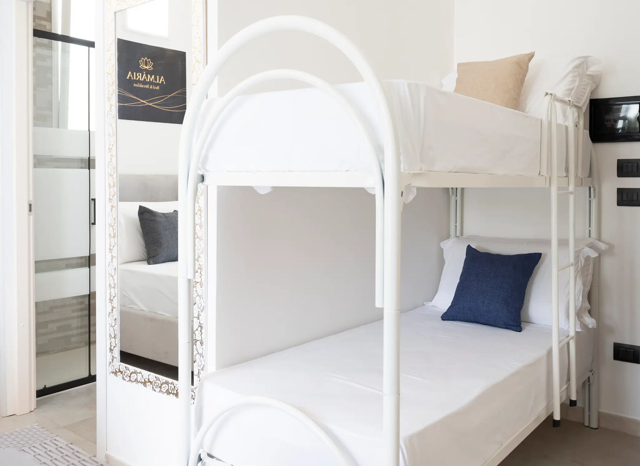 Een stapelbed met een wit frame, een onderste bed met een witte matras, en een bord boven de deur.
