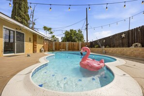 A swimming pool with a pink flamingo float, surrounded by a wooden fence and string lights. - Charming 3BR w/ Hills Views, Pool & Billiards (Hemet)