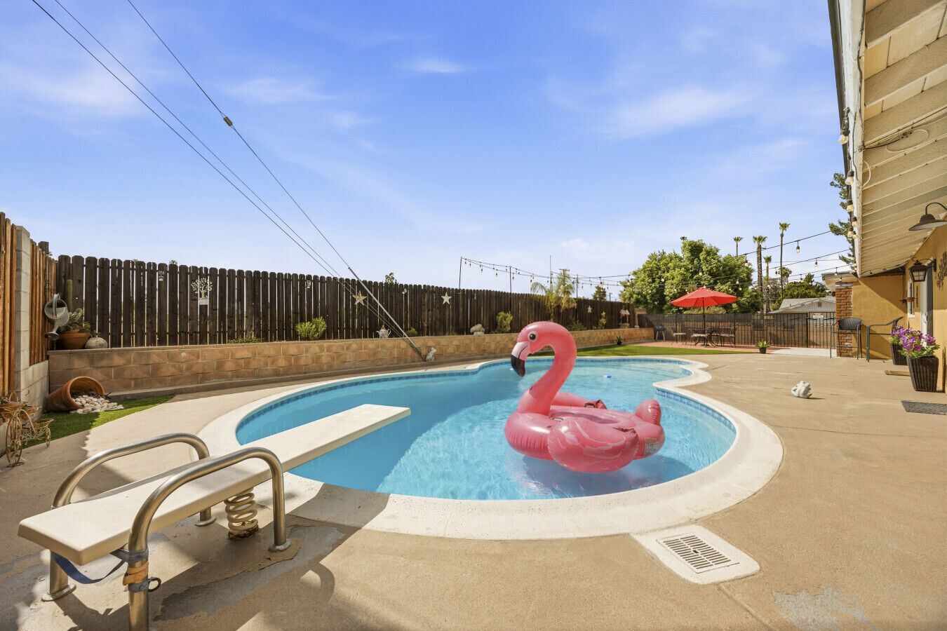A swimming pool with a pink flamingo float, a bench, and a wooden fence in the background.