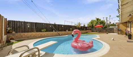 A swimming pool with a pink flamingo float, a bench, and a wooden fence in the background.