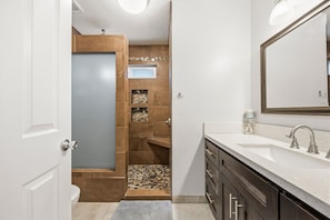 A bathroom with a white vanity, a large mirror, and a shower area with a tiled wall. - Charming 3BR w/ Hills Views, Pool & Billiards (Hemet)