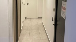 Un pasillo con una puerta a la derecha, un cartel en la puerta y una ventana a la izquierda.