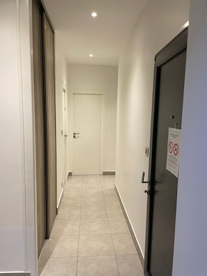 Un couloir avec une porte sur la droite, une pancarte sur la porte et une fenêtre sur la gauche.