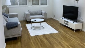 Una sala de estar moderna con un sofá, una mesa de centro, un televisor sobre un mueble bajo y una ventana con persianas.