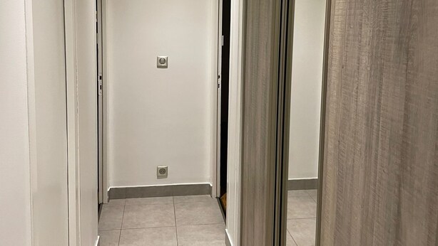 Un pasillo con paredes blancas, suelo de baldosas y una puerta corredera a la derecha.