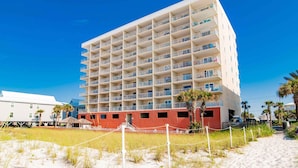 A multi-story hotel with balconies, located on a sandy beach with palm trees. - Seacrest #507 (Gulf Shores)