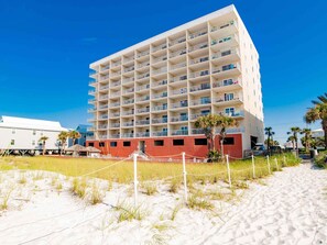 A multi-story hotel with balconies, located on a sandy beach with palm trees. - Seacrest #507 (Gulf Shores)