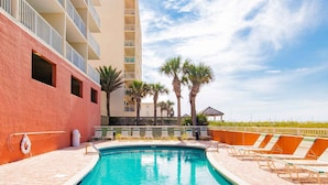 A swimming pool with lounge chairs, palm trees, and a building with balconies. - Seacrest #507 (Gulf Shores)