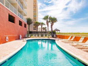 A swimming pool with lounge chairs, palm trees, and a building with balconies. - Seacrest #507 (Gulf Shores)