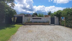 A gravel driveway leading to a gated entrance with a stone wall and a sign reading 'LIS CABANES DES LOUPS'. - Cocoon-style wooden accommodation with breakfasts included (Héloup)