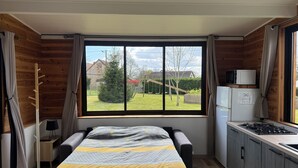 A bedroom with a large window, a bed, a desk, a chair, a wardrobe, and a kitchenette. - Cocoon-style wooden accommodation with breakfasts included (Héloup)