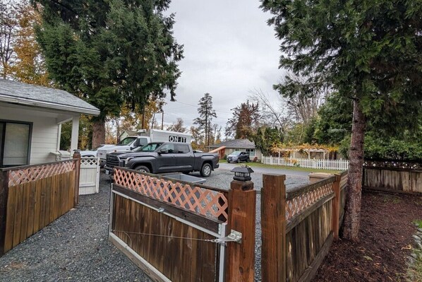 A gated driveway with a wooden fence, a white building, and parked vehicles.