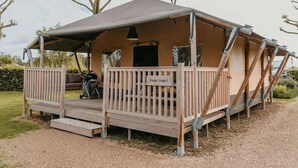 Una estructura tipo tienda señalizada como 'Ranger Lodge 1', con una terraza de madera, un banco y una motocicleta estacionada afuera.
