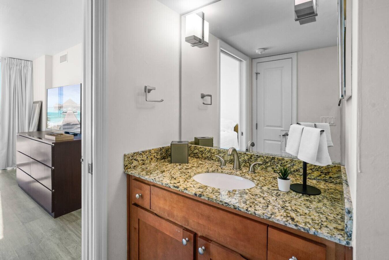 Un baño moderno con encimera de granito, un lavabo, un espejo y un perchero para toallas.