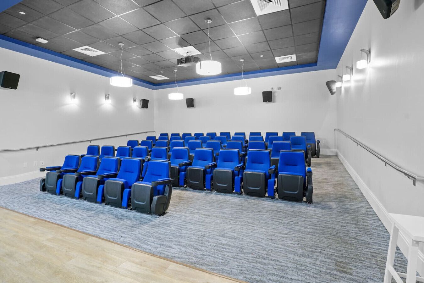 A conference room with rows of blue chairs, a carpeted floor, and a white wall with a blue trim.