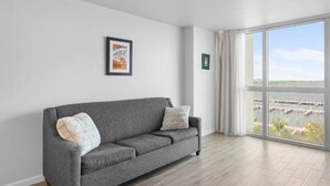 A grey sofa with two pillows, a framed picture on the wall, and a large window with a view of a marina. - Cozy Water Views Apt Fort Myers (Fort Myers)